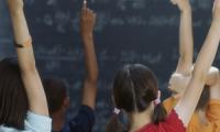 Niñas y niños en un salón de clase levantan la mano para participar