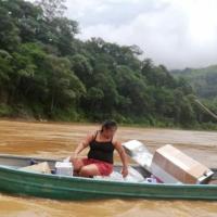 En un bote dos personas cruzan un río con los materiales donados.