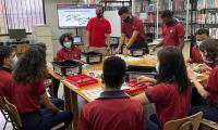 Estudiantes con uniforme con camiseta de color rojo sentados en una mesa redonda discutiendo una lección
