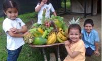Cuatro niños alrededor de una mesa con frutas y verduras que ellos sembraron