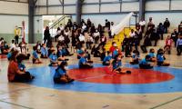 Grupos de niños sentados en el piso de un gimnasio.