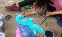 Mujer sentada en el piso pinta una tortuga en colores pasteles